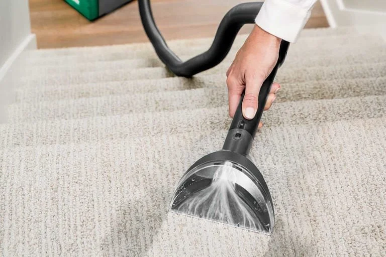 Person using a handheld vacuum to clean a beige carpet.